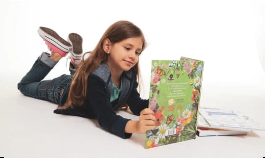 Menina deitada lendo um livro da educação infantil dos sistemas mackenzie de ensino